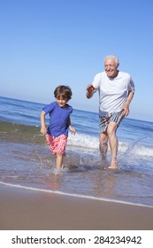 Grandfather Chasing Grandson Along Beach