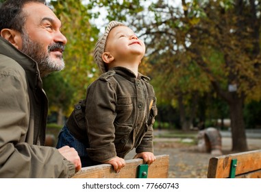 Grandfather and child leaning on bench in the park on autumn day, looking up