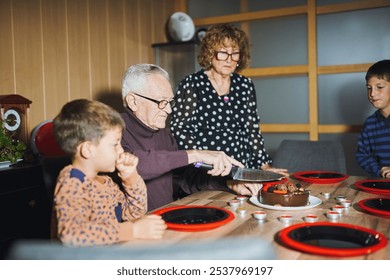 Grandfather cutting birthday cake with family gathered around - Powered by Shutterstock