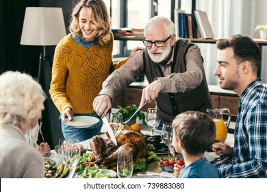 grandfather cutting turkey for family on thanksgiving dinner