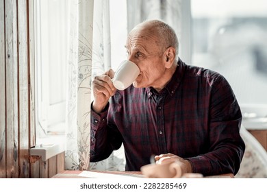 Grandfather drinking coffee or tea from white cup and looking through window. Lonely retired man have breakfast. - Powered by Shutterstock