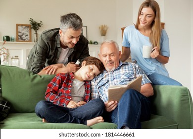 Grandfather enjoying literature together grandson and his young parents at cozy living room. Elderly man reading book aloud to cute schoolboy and his smiling family. Multi-generational family weekend - Powered by Shutterstock