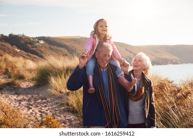 Grandfather Giving Granddaughter Ride On Shoulders As They Walk Through Sand Dunes With Grandmother - Powered by Shutterstock