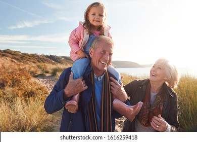 Grandfather Giving Granddaughter Ride On Shoulders As They Walk Through Sand Dunes With Grandmother - Powered by Shutterstock