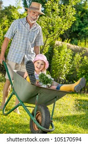 Grandfather Giving Granddaughter Ride In Wheelbarrow In The Garden