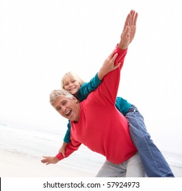 Grandfather Giving Grandson Piggy Back On Winter Beach