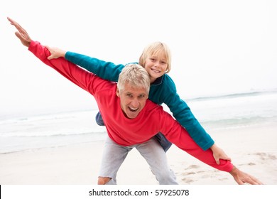 Grandfather Giving Grandson Piggy Back On Winter Beach