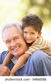 Grandfather Giving Grandson Ride On Back In Park