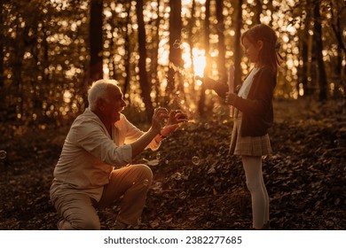 Grandfather and granddaughter enjoying their bonding while they are blowing bubbles and having a picnic in the forest - Powered by Shutterstock