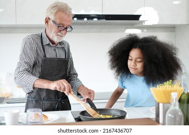 Grandfather And Granddaughter Making Food. Portrait Of Nice Cheerful Kind Grey-haired Grandparent Teaching Grandchild Cooking Homemade. At Modern Light White Interior Kitchen House. Spaghetti.