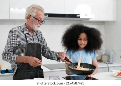 Grandfather And Granddaughter Making Food. Portrait Of Nice Cheerful Kind Grey-haired Grandparent Teaching Grandchild Cooking Homemade. At Modern Light White Interior Kitchen House. Spaghetti.