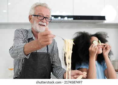 Grandfather And Granddaughter Making Food. Portrait Of Nice Cheerful Kind Grey-haired Grandparent Teaching Grandchild Cooking Homemade. At Modern Light White Interior Kitchen House. Spaghetti.