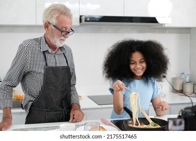 Grandfather And Granddaughter Making Food. Portrait Of Nice Cheerful Kind Grey-haired Grandparent Teaching Grandchild Cooking Homemade. At Modern Light White Interior Kitchen House. Spaghetti.