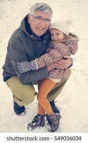 Grandfather and granddaughter posing in the snow. Looking at camera.