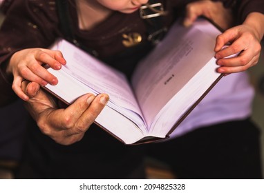 Grandfather and granddaughter read a big book at home library. Close up old hands and kid hands together holding a book focus on hands. Home comfort, hobby education and experience