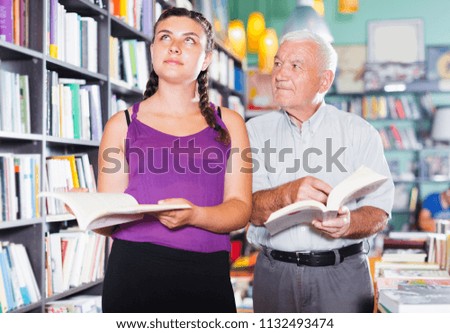 Grandfather with granddaughter are reading books in bookstore