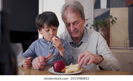 Grandfather and grandson enjoying apple slices, family time, generational connection, shared task, hands-on teaching, cutting fruit, affectionate bond, home setting, healthy snack - Powered by Shutterstock