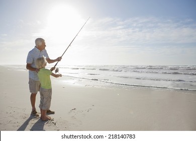 Grandfather And Grandson With Fishing Rod On Sunny Beach