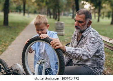 Grandfather And Grandson Fixing Bike For A Ride In Park