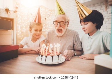 Grandfather, grandson and granddaughter at table at home. Grandpa is blowing candles on birthday cake. - Powered by Shutterstock