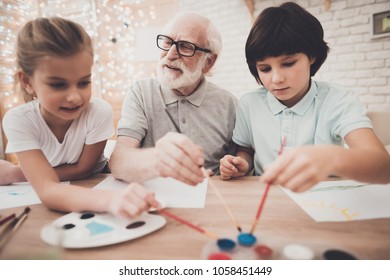 Grandfather, Grandson And Granddaughter At Table At Home. Children Are Painting.