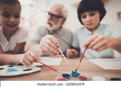 Grandfather, Grandson And Granddaughter At Table At Home. Children Are Painting.