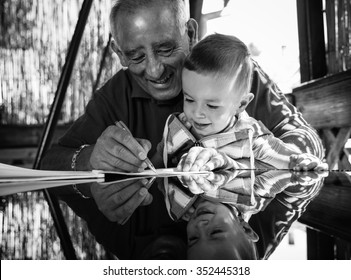 Grandfather And Grandson Having Fun Drawing Something On Paper On A Glass Table That Reflects Their Faces.Black And White.