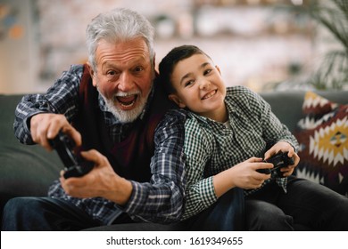 Grandfather and grandson playing video game with joysticks in living room while sitting on couch. 
Grandfather and grandson are playing video games at home.  - Powered by Shutterstock