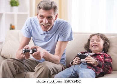 Grandfather and grandson are playing video games at home.