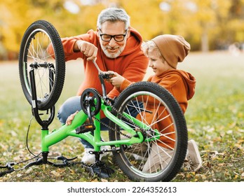 grandfather and grandson repair a bicycle together outdoors in the autumn park - Powered by Shutterstock