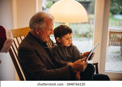 Grandfather and grandson sitting on chair and looking at digital tablet during christmas. Senior man with a kid having a video call on digital tablet. - Powered by Shutterstock