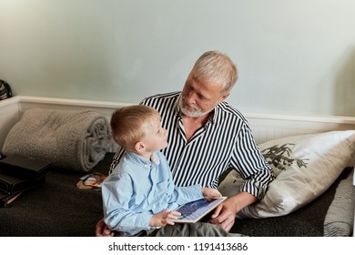 Grandfather And Grandson Using Digital Tablet For Surfing Internet And Playing Game In Living Room