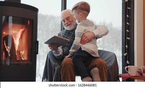 Grandfather And Grandson Using Digital Tablet For Surfing Internet And Playing Game Near The Fireplace At Home Grandpa Adult Grandchild Child Childhood Communication Computer Slow Motion