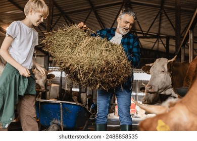 Grandfather and grandson working together, feeding cows in a barn, highlighting family involvement on an organic farm. - Powered by Shutterstock