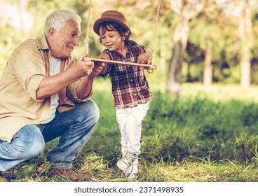 Grandfather helping his grandson to get on a swing in a outdoor park - Powered by Shutterstock