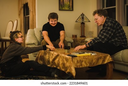 Grandfather and his adult grandchildren playing cards in  living room in evening - Powered by Shutterstock