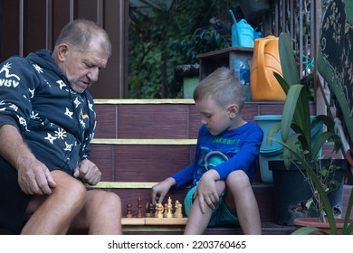 Grandfather With His Grandson Playing Chess Outside. 