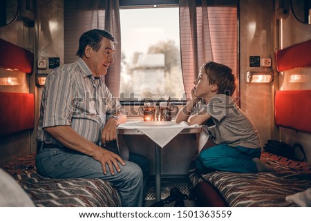 Grandfather with his grandson in the russian train drinking tea from traditional russian cups with cupholders. Image with selective focus and toning. 