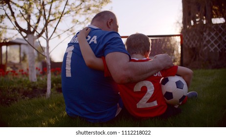 Grandfather Is Hugging His Grandson Holding Soccer Ball In His Hand On Sunset