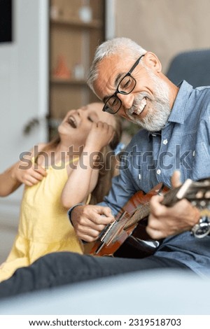 Grandfather laughing as his granddaughter pretends to play guitar with him
