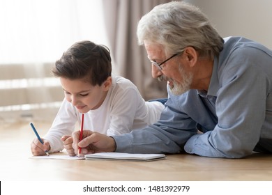 Grandfather lying on warm floor with little grandson, grandad helps to little grandkid teaches him to draw using colored pencils on paper activity at home, younger older generations connection concept - Powered by Shutterstock