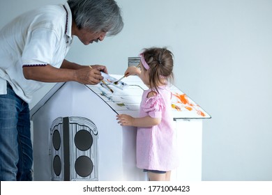 Grandfather Painting With Cute Little Girl On Toy Cardboard House