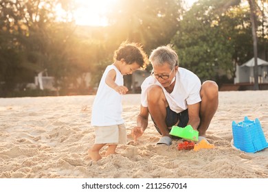 Grandfather playing with grandson on the beach. Happy Senior man and cute boy building sand castle on the sea beach.