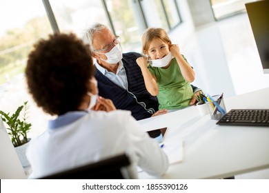 Grandfather With Protective Facial Masks With Cute Granddaughter At Black Female Doctor