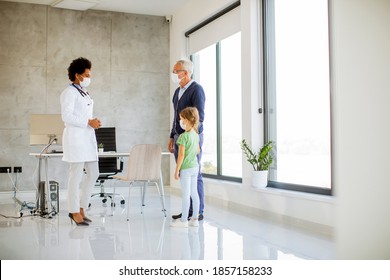 Grandfather With Protective Facial Masks With Cute Granddaughter At Black Female Doctor