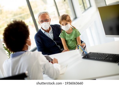 Grandfather With Protective Facial Masks With Cute Granddaughter At Black Female Doctor