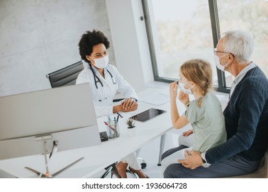 Grandfather With Protective Facial Masks With Cute Granddaughter At Black Female Doctor