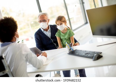 Grandfather With Protective Facial Masks With Cute Granddaughter At Black Female Doctor