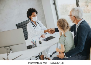 Grandfather With Protective Facial Masks With Cute Granddaughter At Black Female Doctor