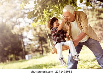 Grandfather pushing his grandson on the swing in a outdoor park - Powered by Shutterstock